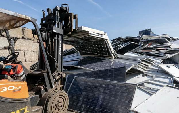 A forklift next to a pile of discarded solar panels