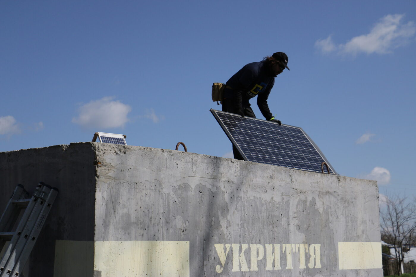 A man fixes a solar panel on the roof of a concrete shelter