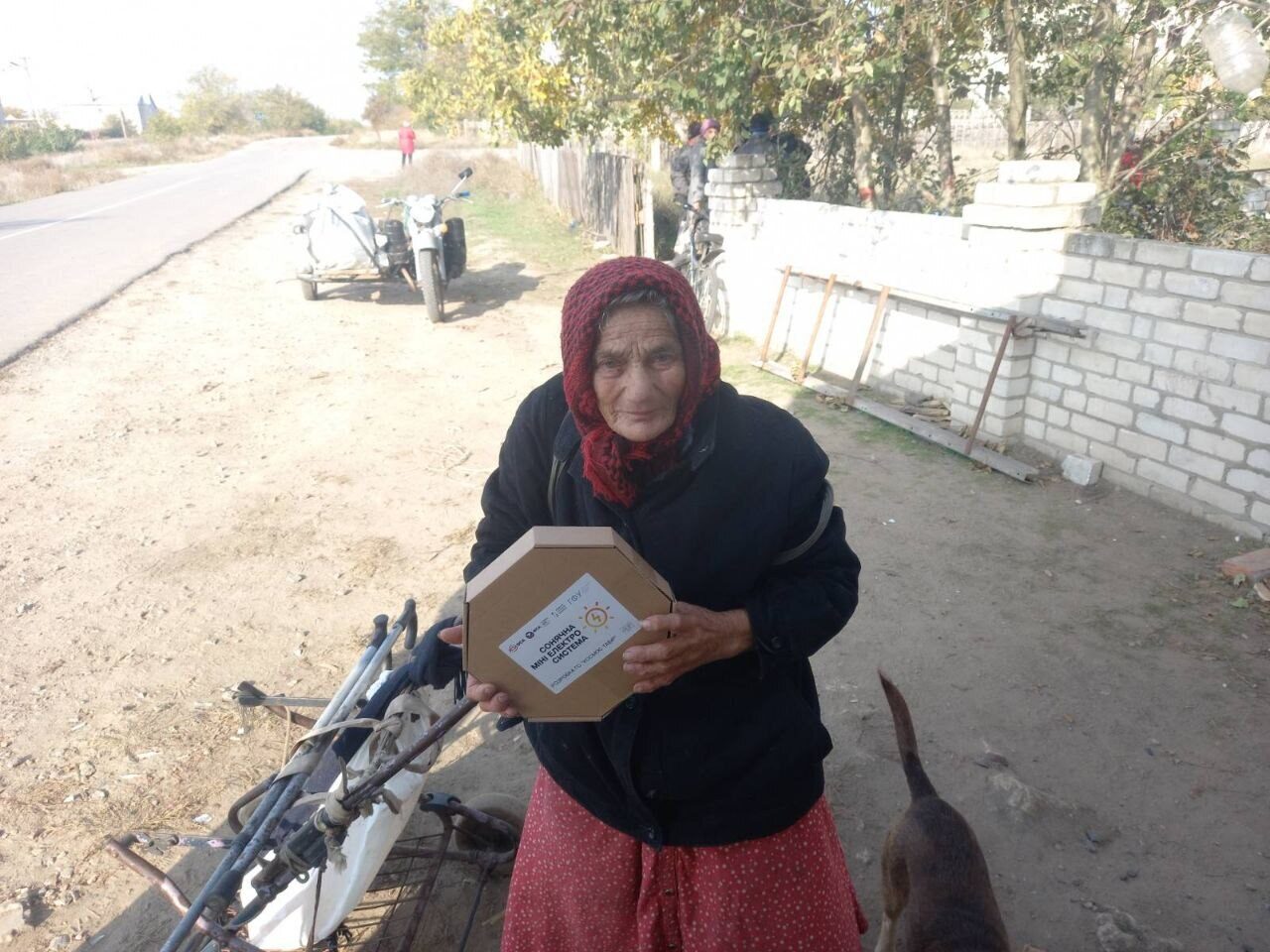 An elderly woman in a headscarf holds a MINISOLAR box