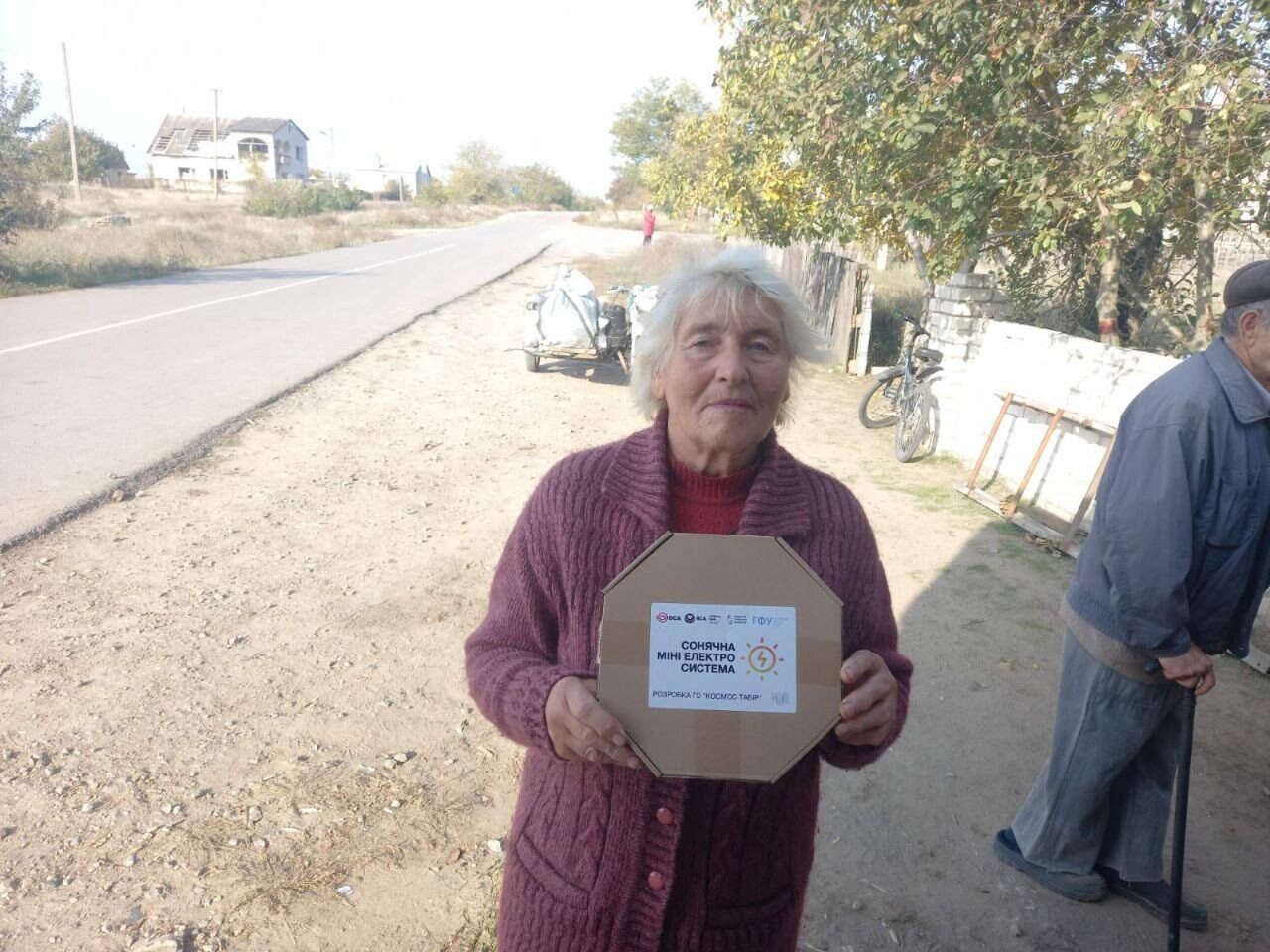 An elderly woman in a red jacket holds a MINISOLAR box