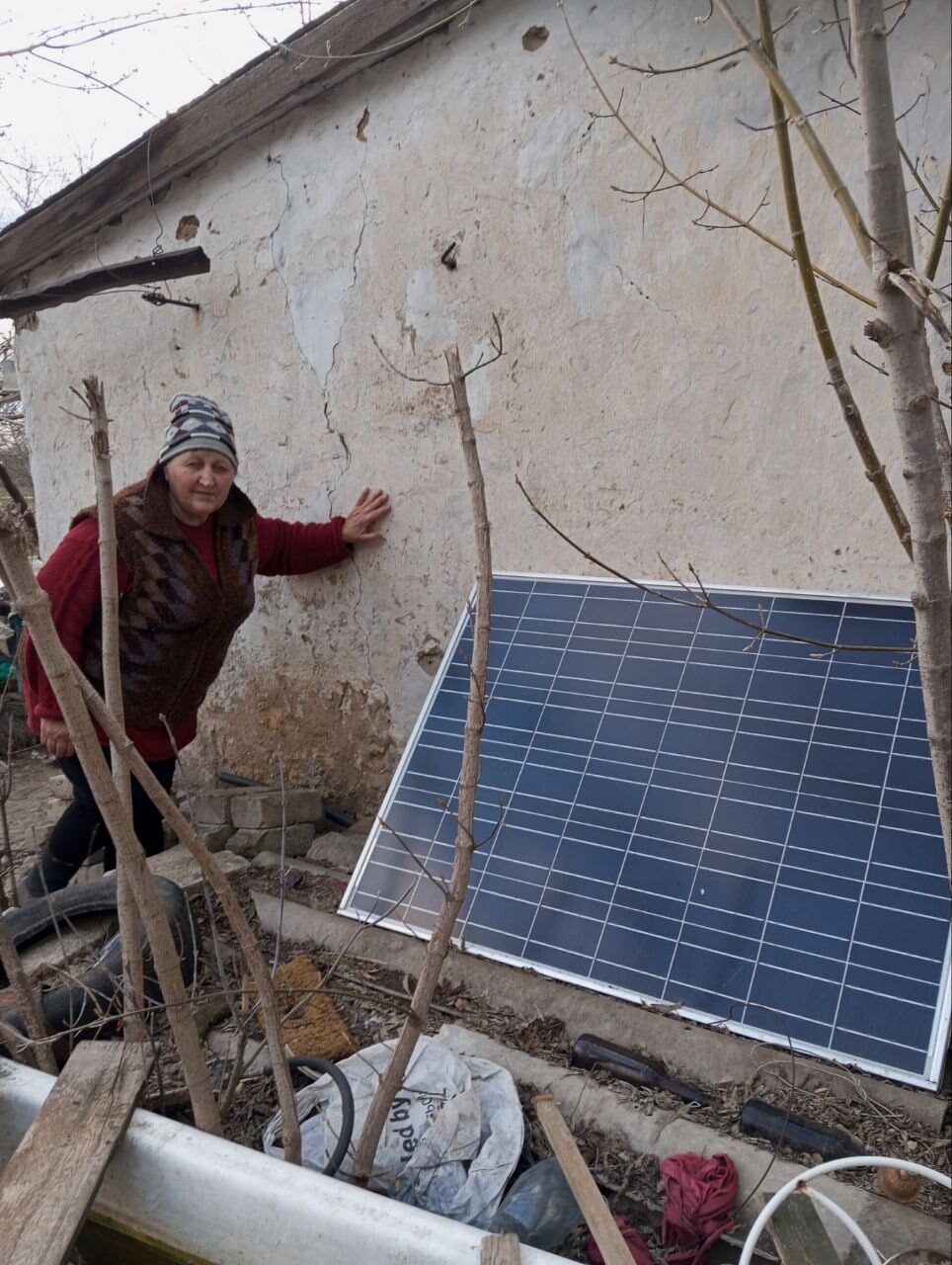 A woman stands by a damaged wall next to a solar panel