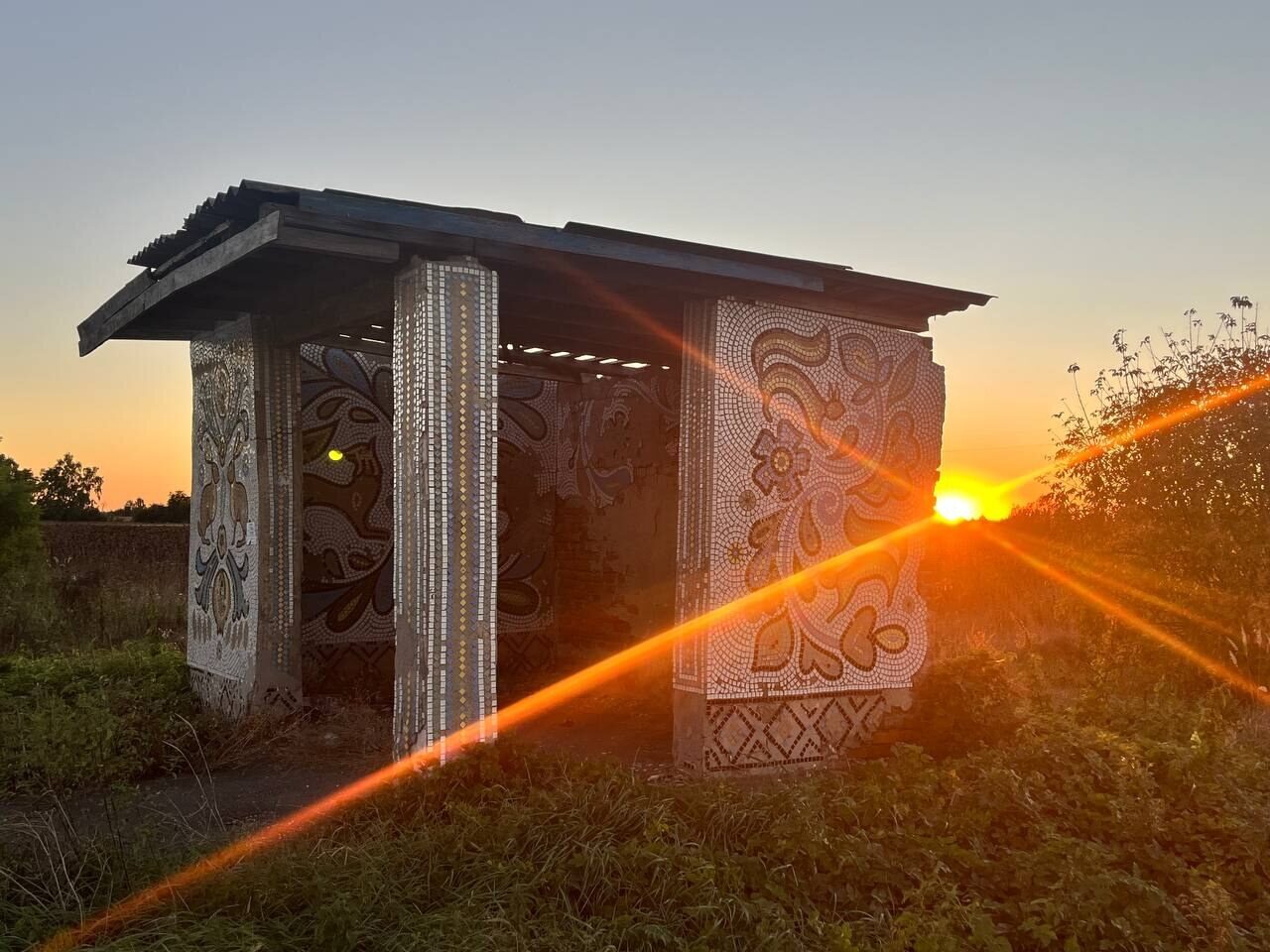 Sunrise behind a bus stop decorated with mosaic