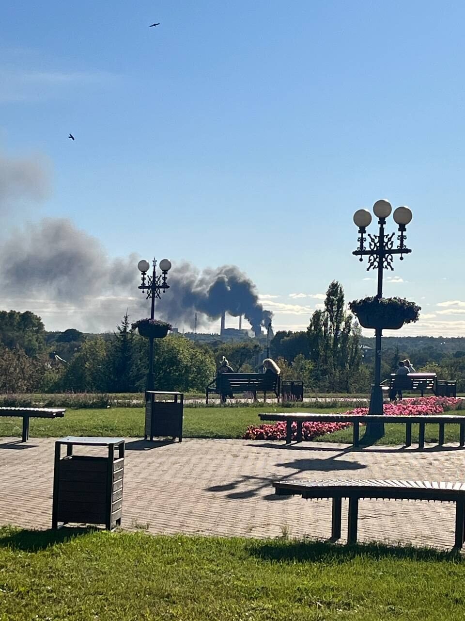 Smoke rises behind a park with street lamps
