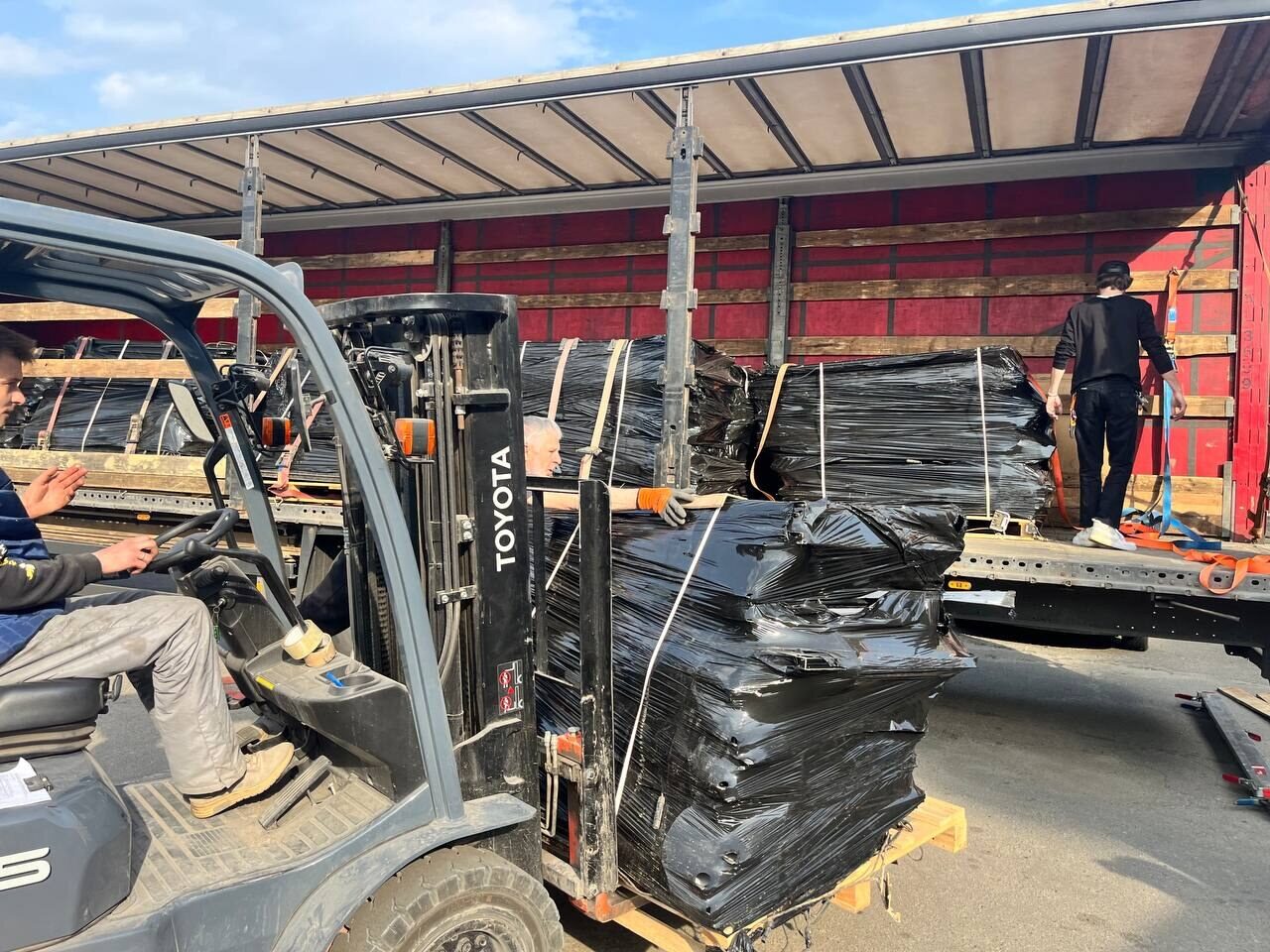 A forklift unloads wrapped panels from a truck