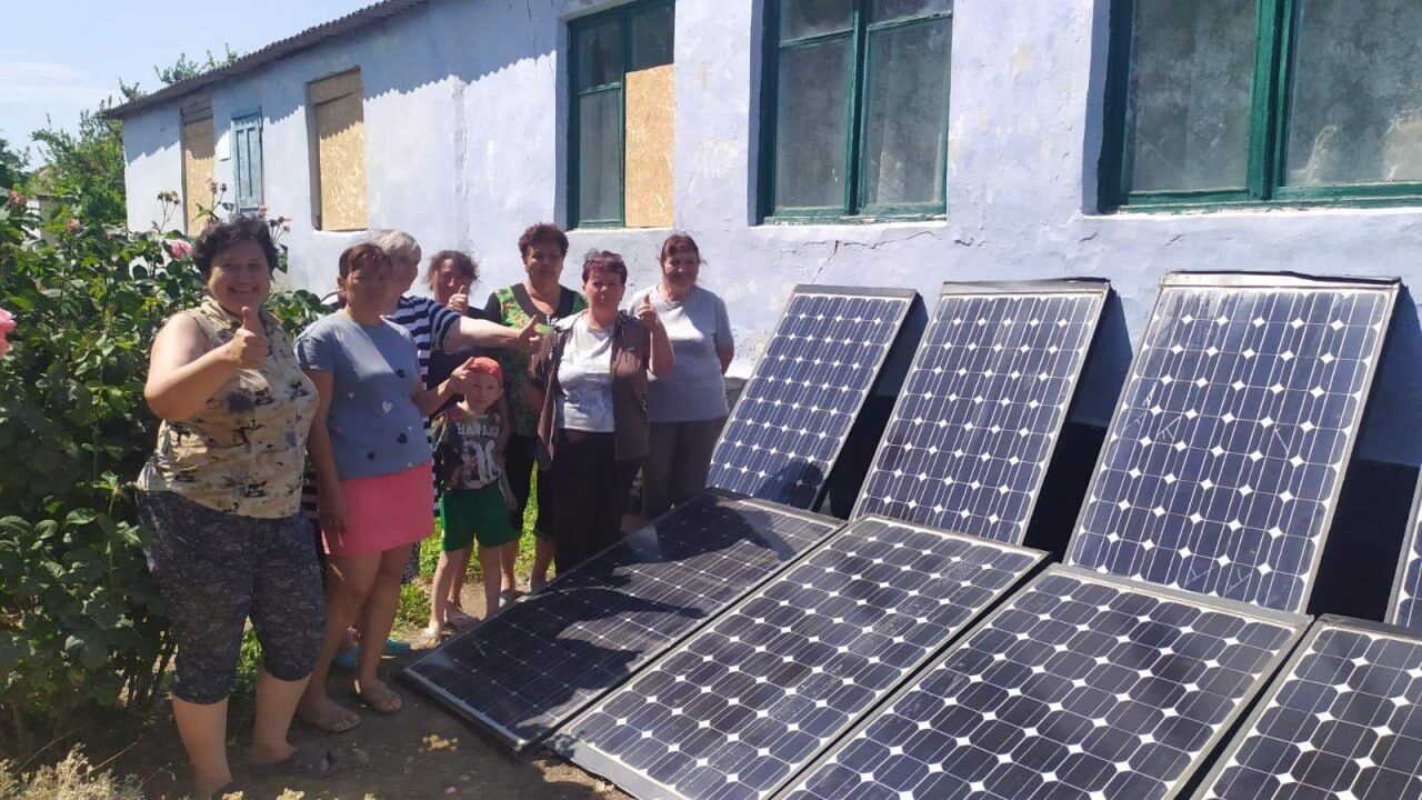 A group of villagers stands next to a row of solar panels