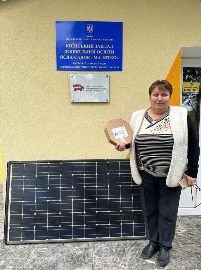A woman stands next to a solar panel outside a kindergarten